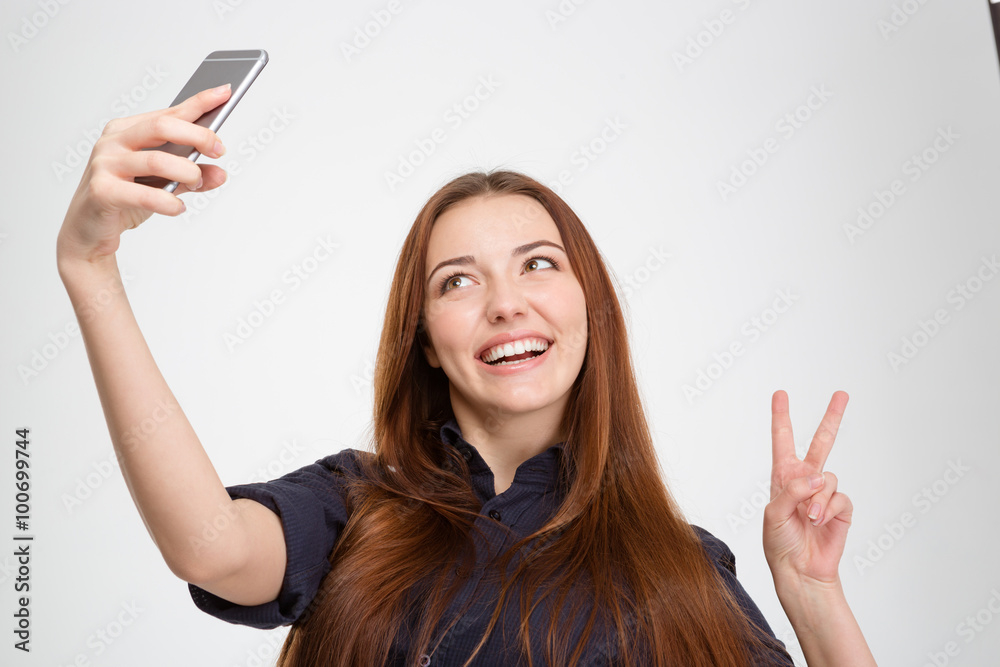 Smiling woman taking selfie with mobile phone showing victory sign Smiling woman taking selfie with mobile phone showing victory sign