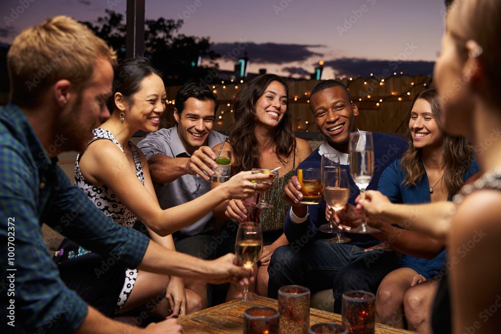 Group Of Friends Enjoying Night Out At Rooftop Bar - obrazy, fototapety, plakaty 
