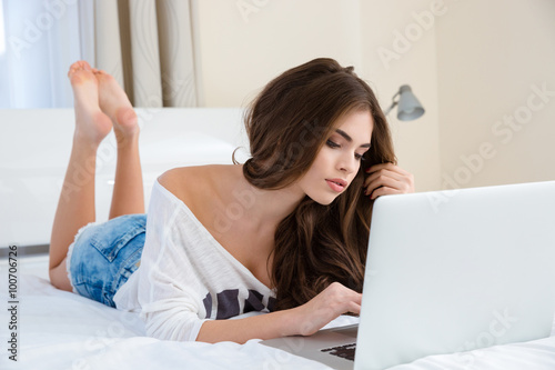 Pensive lovely young woman using laptop and thinking