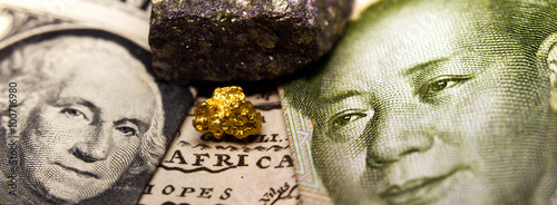 Close-up of a gold nugget / rare earth metal in between a 1 dollar note (showing George Washington) and Mao on a 1 yuan Chinese banknote  on top of an old map of Africa photo