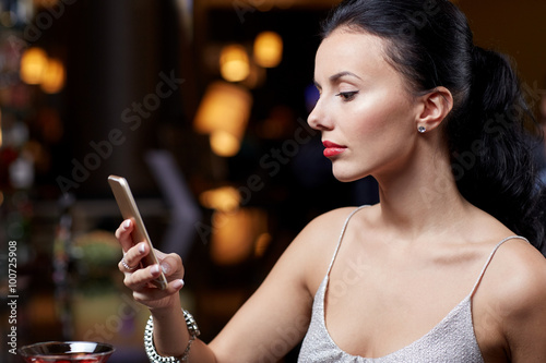young woman with smartphone at night club or bar