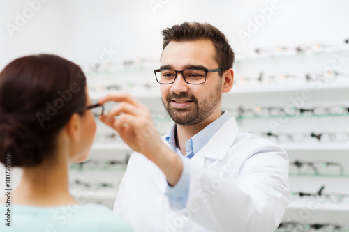 Fotografie optician putting glasses to woman at optics store