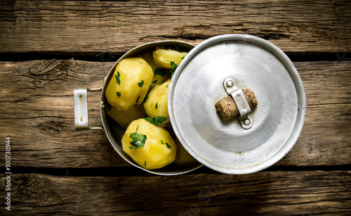 Boiled potatoes with herbs in an old pot on a wooden table .