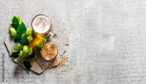 Beer, green hops and malt on stone surface.