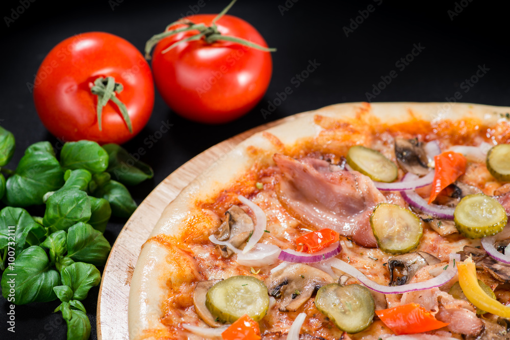 closeup Tasty pizza with mushrooms, ham and pickles on a black b closeup Tasty pizza with mushrooms, ham and pickles on a black b
