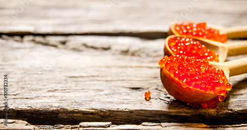 Red caviar in a wooden spoon. On wooden background.