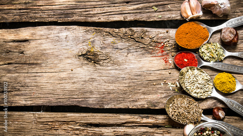 Different kinds of spices in spoons. On wooden background.
