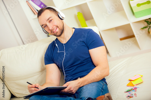 Handsome young man at home writing on notebook, sitting on couch, listen to music © Mediteraneo