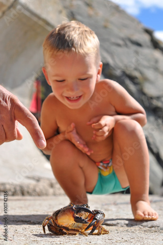 tanned boy looks at the crab.