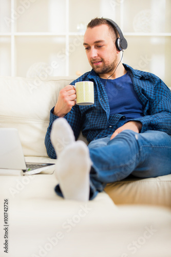 Handsome man sitting on sofa with laptop drinking tea
