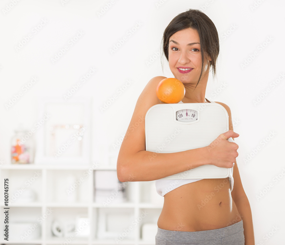 Girl holding an orange on top of a measuring scale in her hands Girl holding an orange on top of a measuring scale in her hands