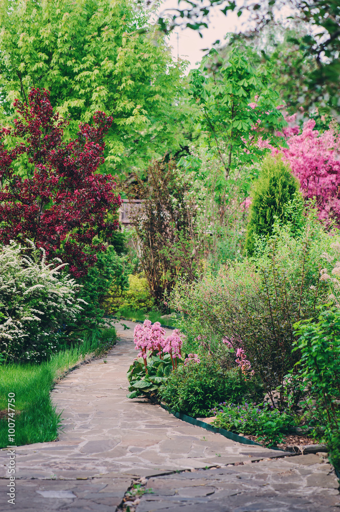 English garden in spring. Beautiful view with blooming trees and shrubs. Stone pathway.