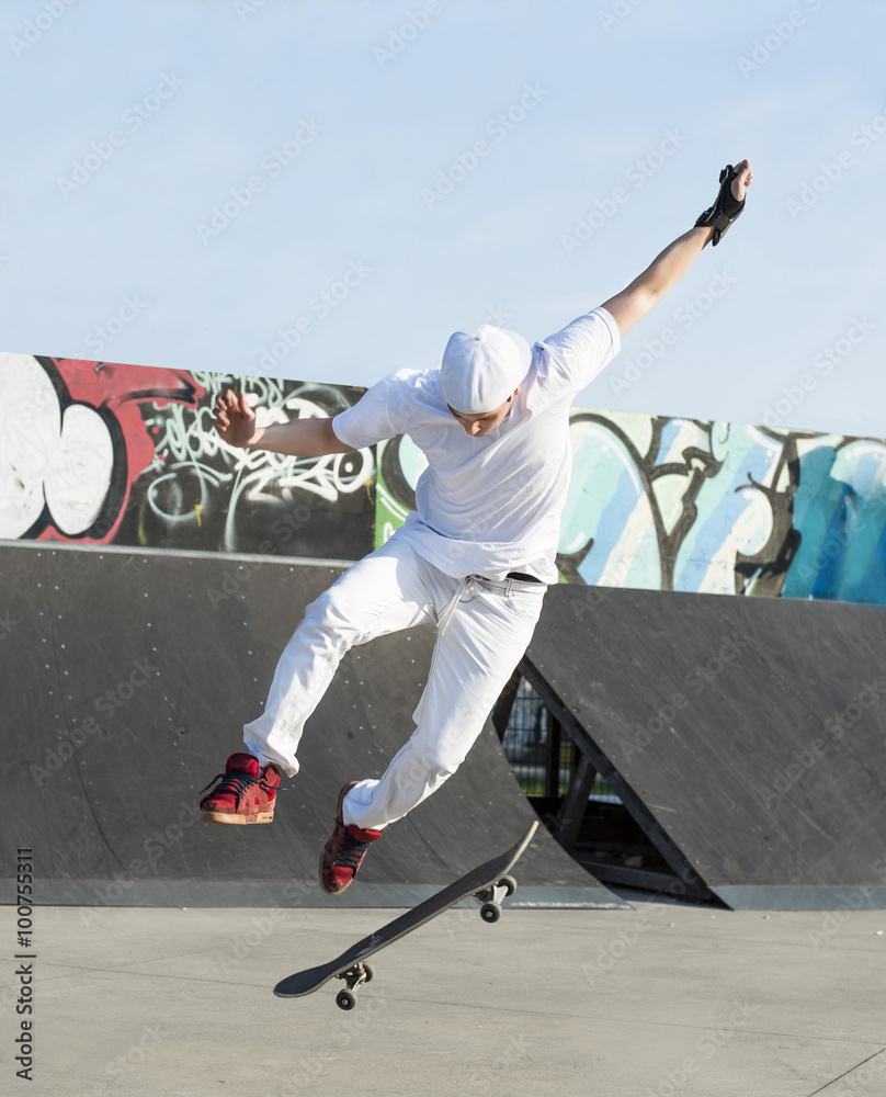 Fototapeta Skateboarder doing a jumping trick at skateboard park