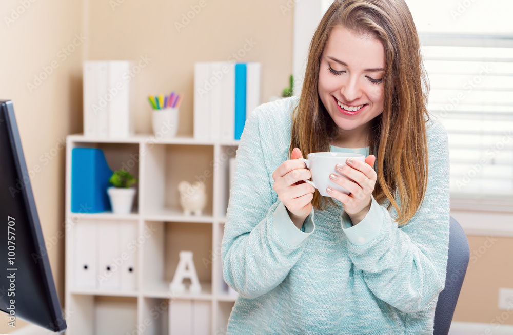 Happy young woman drinking coffee in her home office Happy young woman drinking coffee in her home office