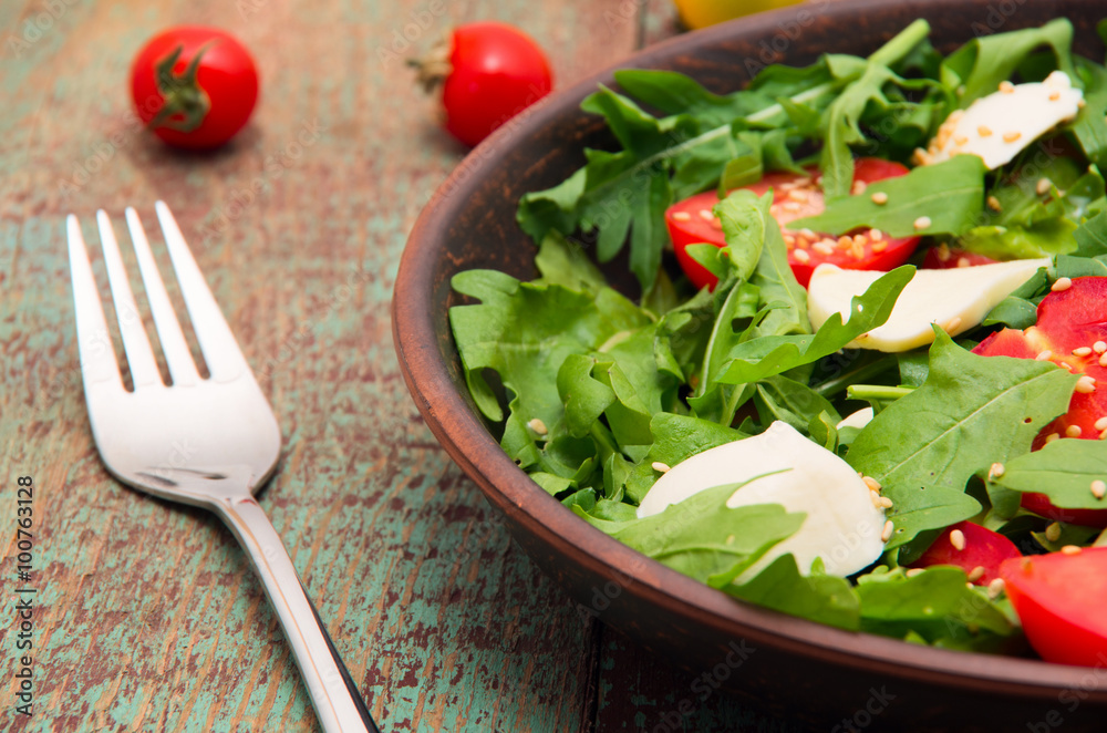 Green salad made with arugula, tomatoes, cheese mozzarella balls and sesame on plate Green salad made with arugula, tomatoes, cheese mozzarella balls and sesame on plate