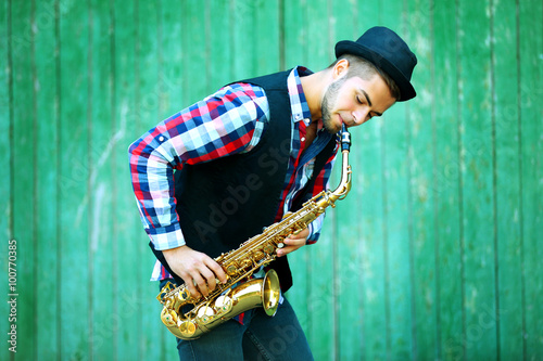 Canvas Print Young man playing on saxophone outside near the old wall