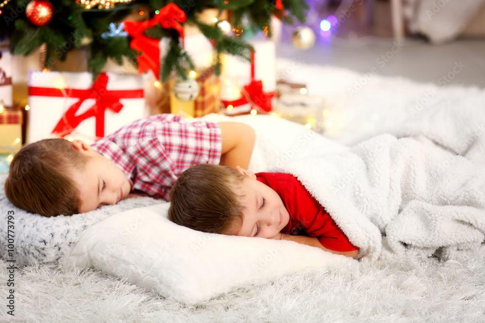 Two cute small brothers sleeping on carpet against Christmas tree