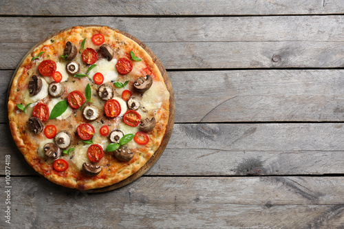 Tasty fresh pizza decorated with mushrooms and tomatoes on wooden background, close up