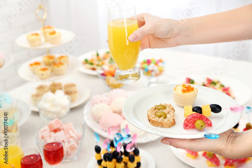 Woman holding glass of juice and plate with snacks on buffet background