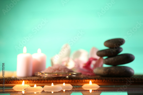 Photography Spa still life with stones, candles and flowers in water on turquoise blurred ba