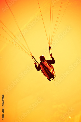 Obraz na płótnie A man flying a paraglider holds steering cables in his hand, orange sky w salonie