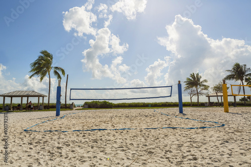 A beach volleyball net on a sunny beach, with palm trees