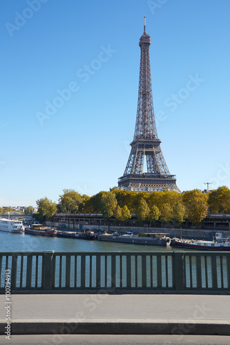Eiffel tower and empty sidewalk bridge on Seine river in a sunny day
