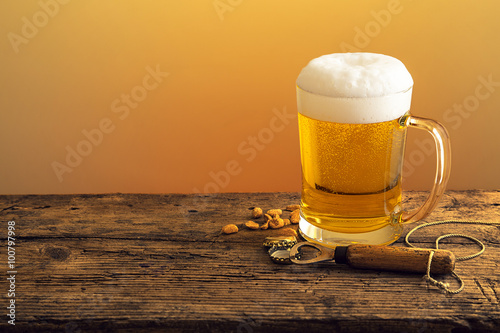 Bierkrug mit Bier und Schaumkrone mit Flaschen  ffner auf Holztheke