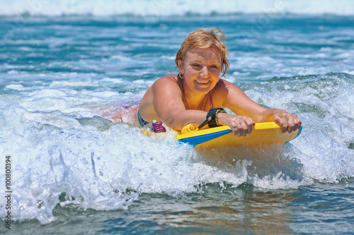 Joyful middle age woman - surfer with bodyboard surfing with fun on small sea waves. Active family lifestyle, people outdoor water sport lesson and swimming activity on summer vacation in ocean island © Tropical studio