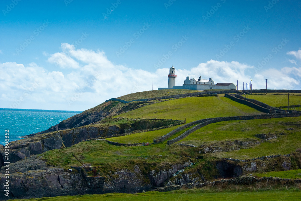 Irish cliff with greenery and a lighthouse in the distance - Coastline of Cork