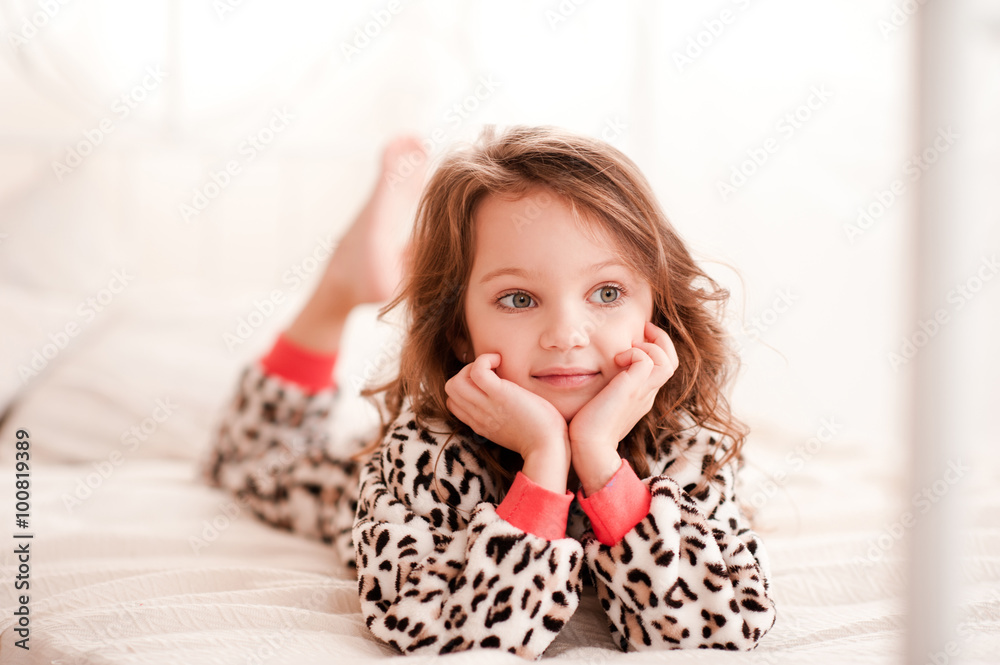 Smiling kid girl 5-6 year old lying in bed wearing leopard print pajamas in room. Looking away. Childhood. Resting in bed. Bed time. Smiling kid girl 5-6 year old lying in bed wearing leopard print pajamas in room. Looking away. Childhood. Resting in bed. Bed time.
