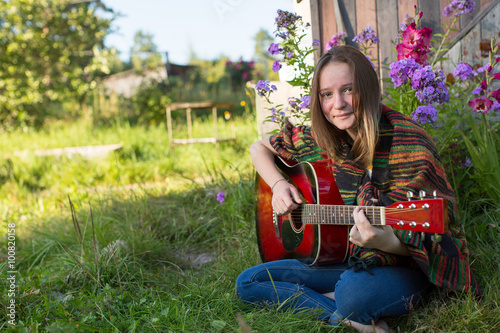 Young girl playing acoustic guitar, outdoors.