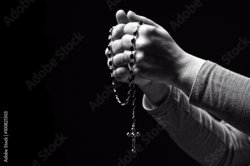 christian rosary in hands. black background. faith, religion, belief