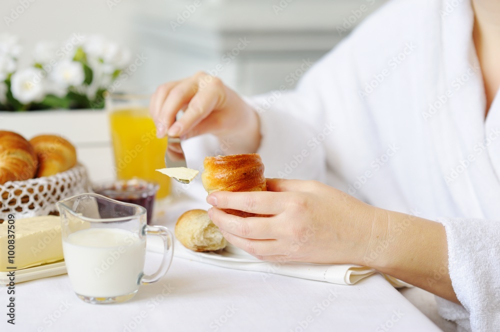 Beautiful woman behind a white table spreads butter croissant. Beautiful woman behind a white table spreads butter croissant.