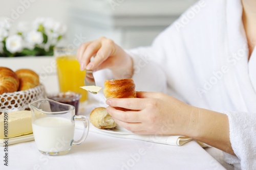 Beautiful woman behind a white table spreads butter croissant.