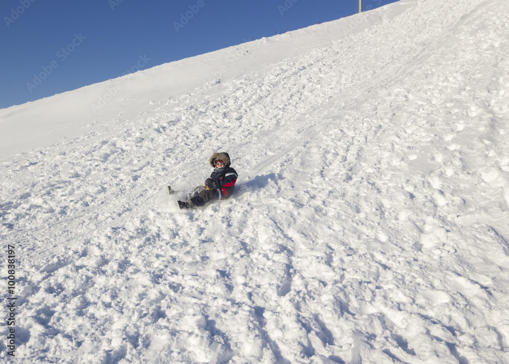 Child on sled going off the winter slope on a sunny day