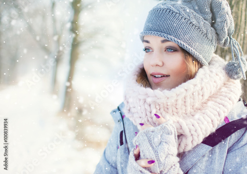 Beautiful young woman wearing winter hat gloves and scarf covered with snow flakes. Winter forest landscape background