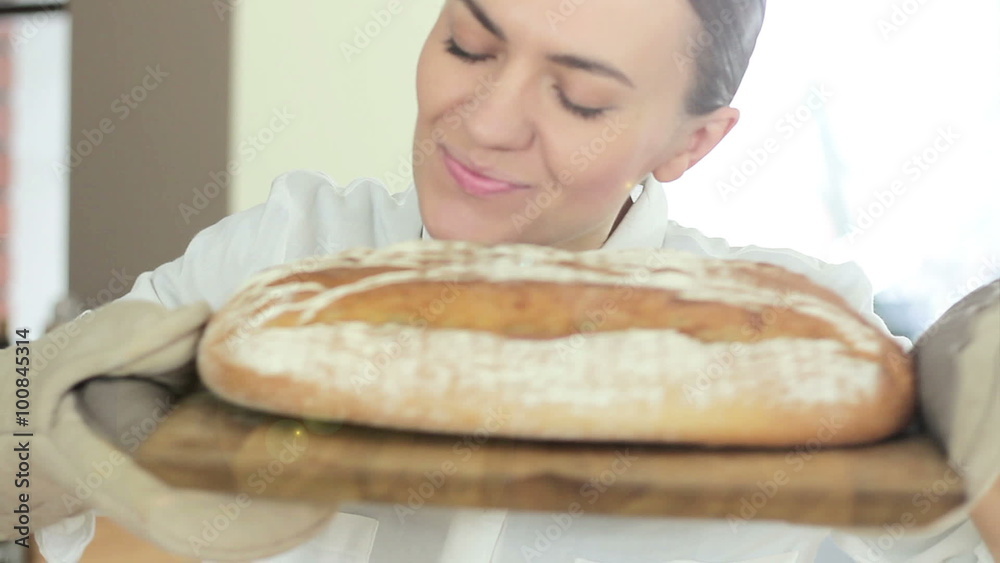 A young smiling woman standing in her kitchen holding freshly baked bread, close up A young smiling woman standing in her kitchen holding freshly baked bread, close up