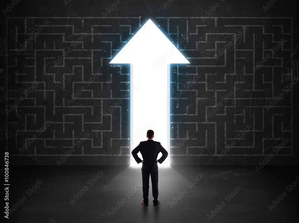 Business person looking at maze with solution arrow on the wall Business person looking at maze with solution arrow on the wall