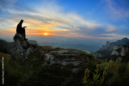 silhouette of priest reading in the sunset light, Romania, Ceahl