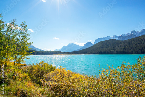 turquoise waters of a lake in front of a forest and a peak in the rocky mountains of alberta canada