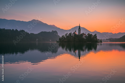 Little Island with Catholic Church in Bled Lake, Slovenia at Sunrise with Castle and Mountains in Background
