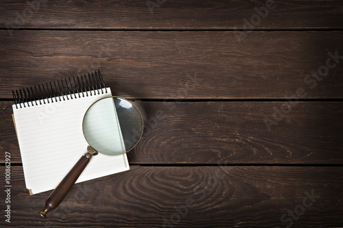 notebook with a magnifying glass on a wooden background