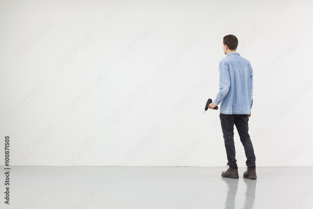 Man holding a drilling machine standing in front of a white wall Man holding a drilling machine standing in front of a white wall