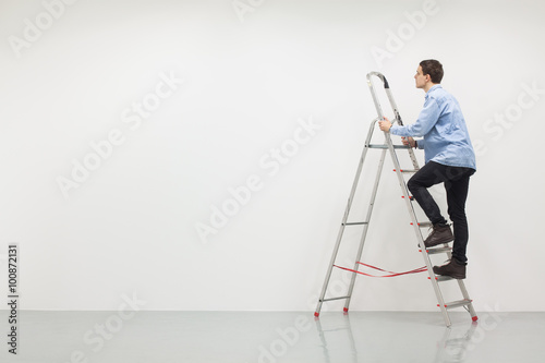 Man climbing a ladder with white wall, construction site