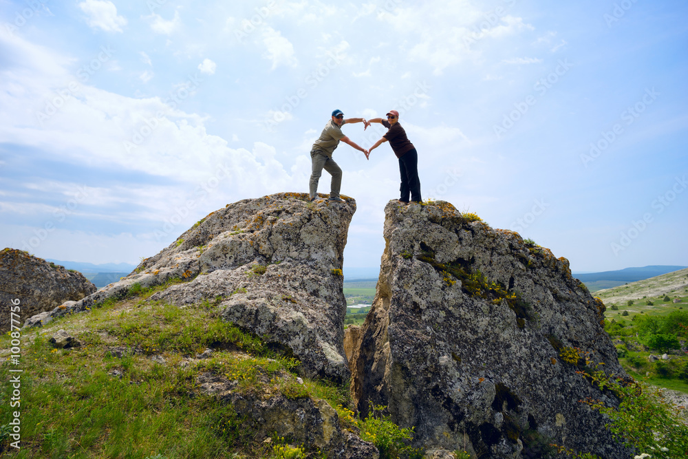 man and the woman folded her hands in a heart shape , standing high on  mountain .