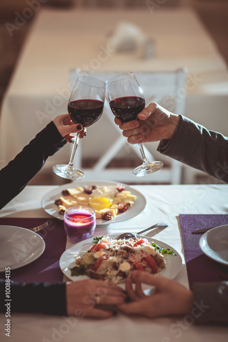 A young couple in love holds hands and raises their glasses with red wine