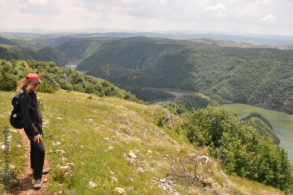 Young woman hiking in nature and looking the scenic view of River Uvac on a sunny summer day