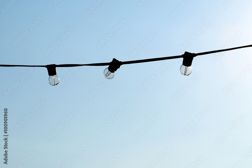 Light bulbs hanging on a electricity wire in clear blue sky background Light bulbs hanging on a electricity wire in clear blue sky background