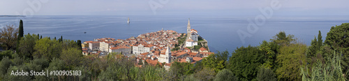 Piran (Italian: Pirano) old town in Slovenia, Gulf of Piran on the Adriatic Sea..Panoramic view of the city. Natural green environment, blue sky, red roofs of houses and Church of Saint George .